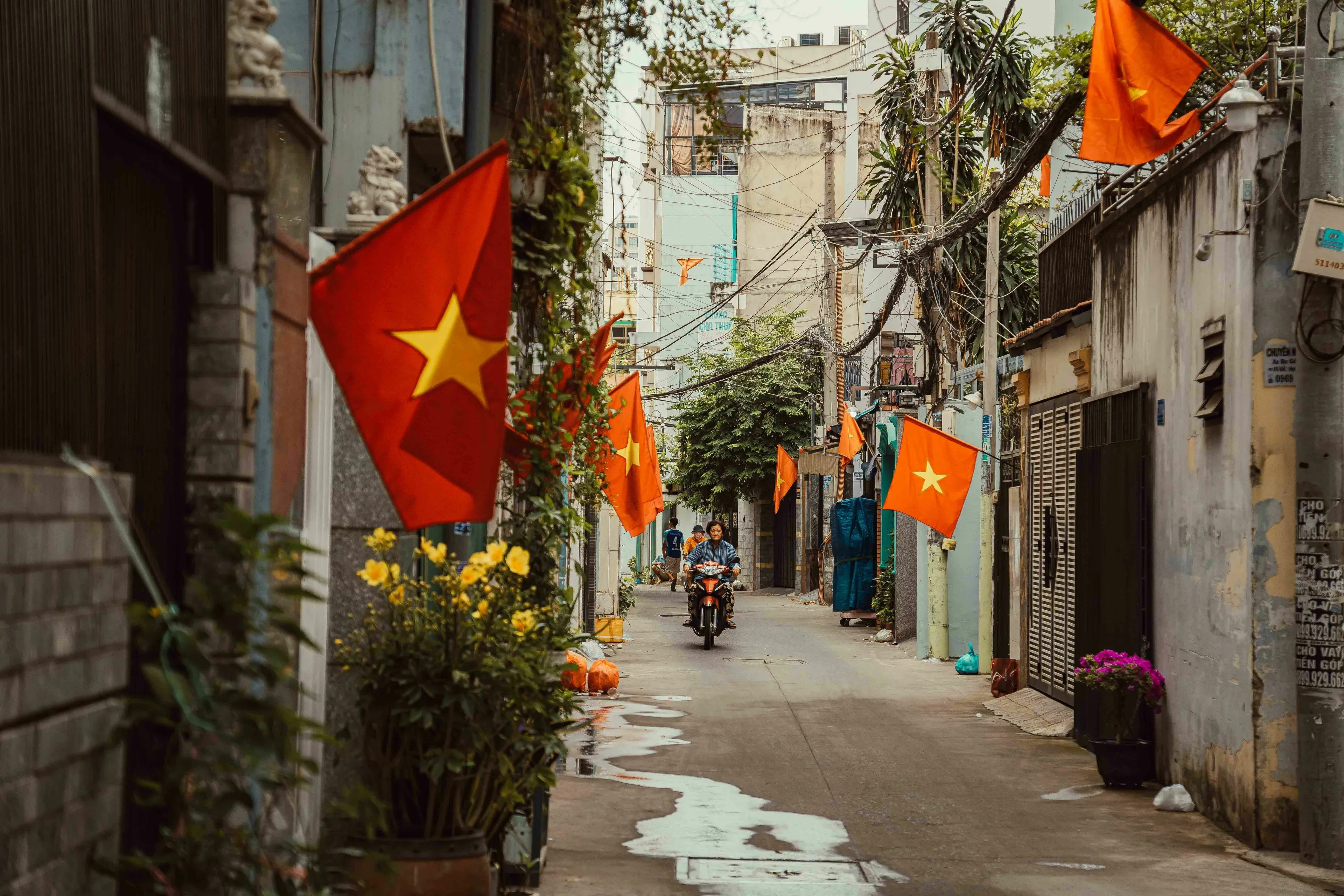 Street scene in Vietnam with flags, a person on a motorcycle, and buildings. General Geography Knowledge Quiz.