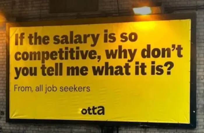 A billboard sign asks, If the salary is so competitive, why don't you tell me what it is? disturbing levels of dystopia in the USA.