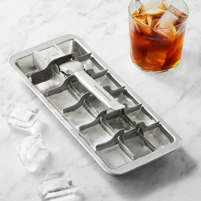 Metal ice cube tray and glass cold drink on marble surface