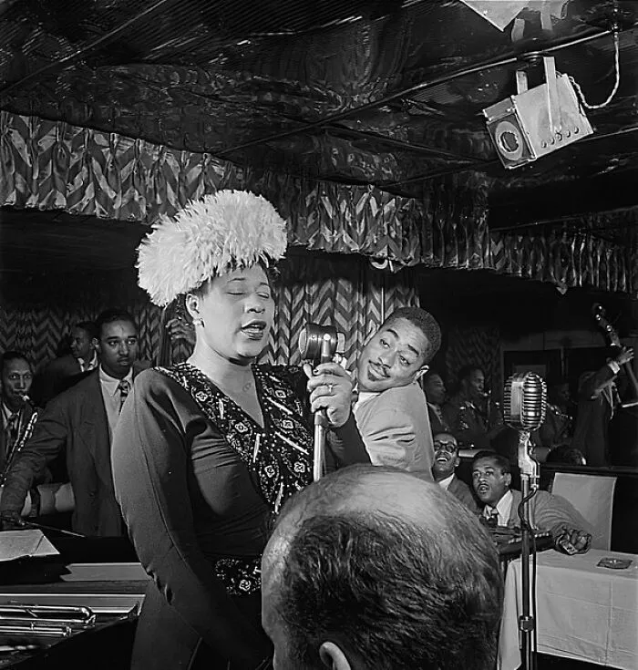 A woman in history, Ella Fitzgerald, sings into a microphone on stage, captivating her audience.