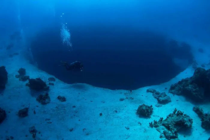 Scuba diver exploring a massive deep blue sinkhole discovered at the bottom of the ocean