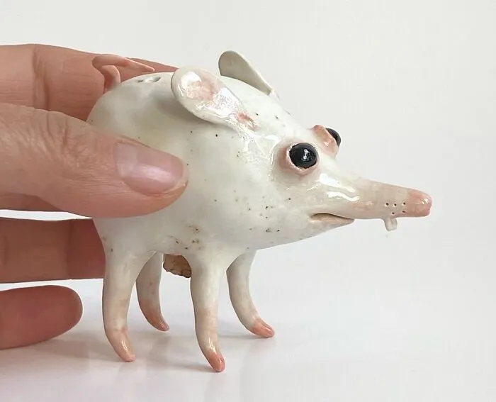 Hand holding a weird ceramic sculpture of a tiny, four-legged white creature with a long snout.