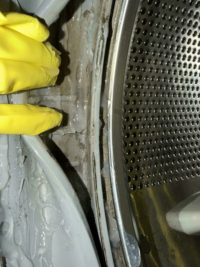 Close-up of dirty washing machine drum with peeling seal and yellow gloves exposing Airbnb fails
