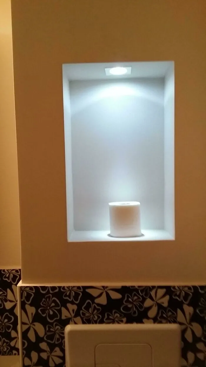 Toilet paper roll displayed alone in a small spotlight niche in hotel bathroom