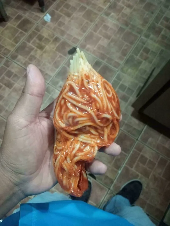 Spaghetti wrapped in plastic wrap held in a hand as a questionable food combo.