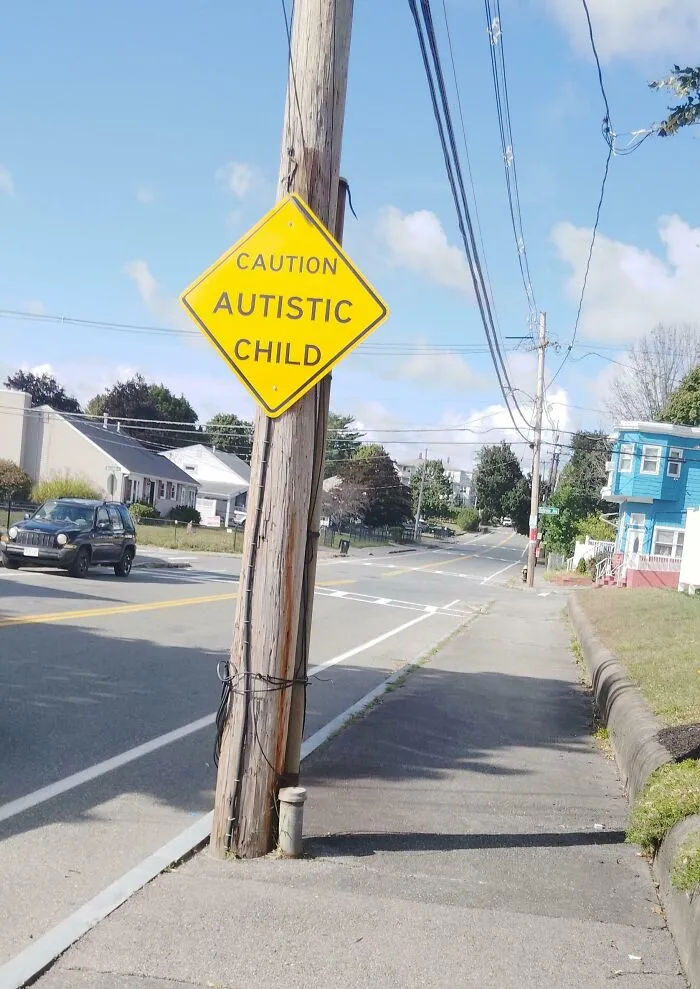A yellow diamond caution sign on a wooden post saying Autistic Child, which looks like a mistake.