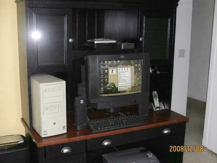 A desktop computer with a beige tower and black monitor on a wooden hutch desk in the early 2000s.