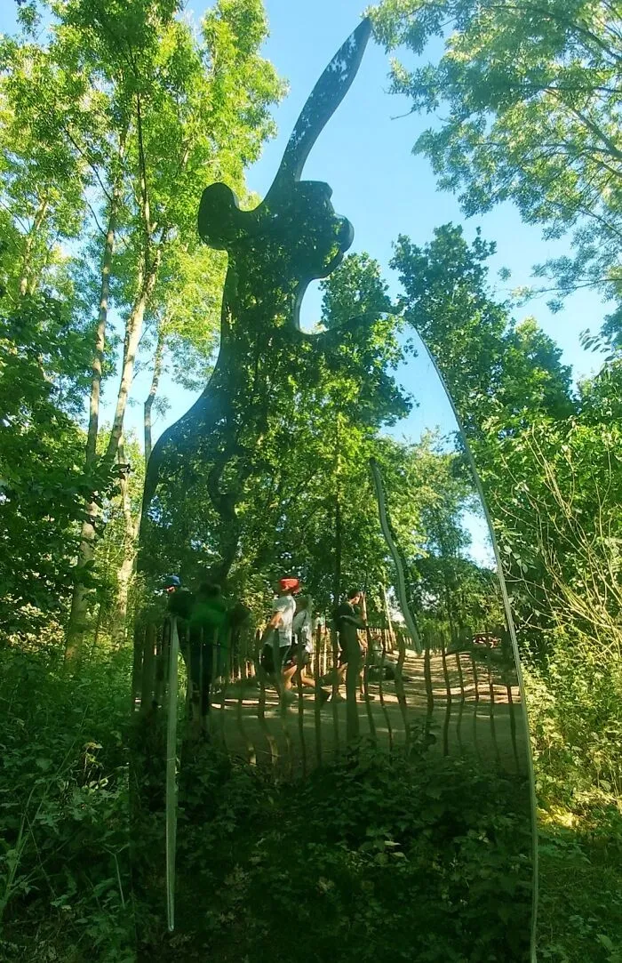 Reflective sculpture of a person with knife blending into bright forest scene