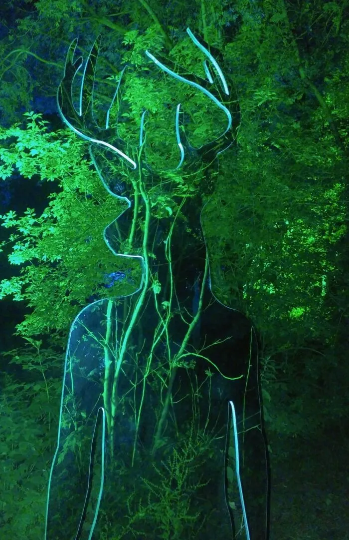 Reflective sculpture shaped like a deer blending with green forest at night