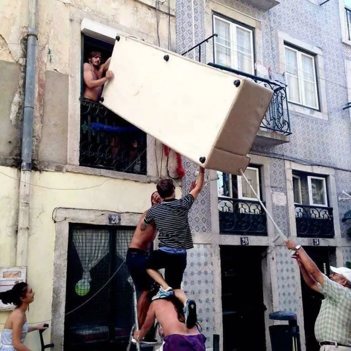 People struggling to move a large couch out of a window in a moving fails scenario