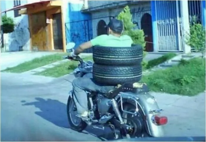 Motorcycle rider carrying two large tires, illustrating a moving fails scenario.