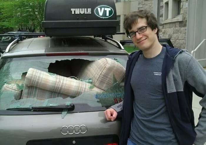 Moving fails image of man smiling next to car with smashed rear window from moving couch