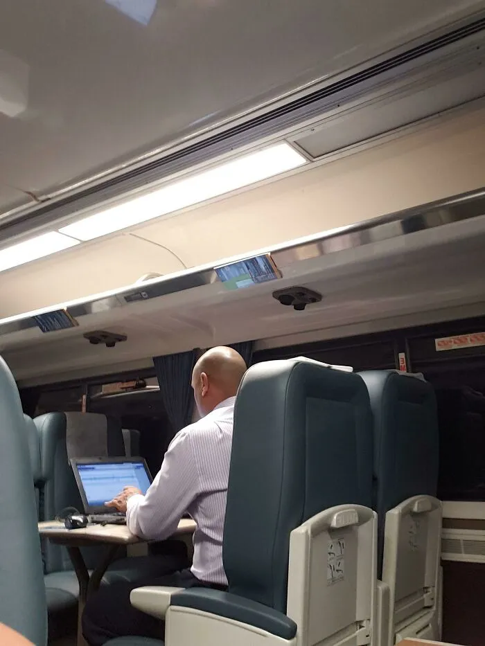 A man working on his laptop on a train, displaying typical public transport interactions