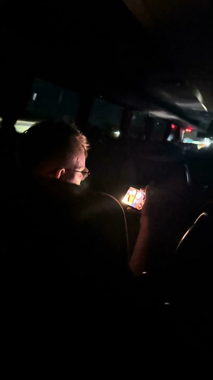 A passenger watching a bright screen on a dark bus, demonstrating public transport interactions.