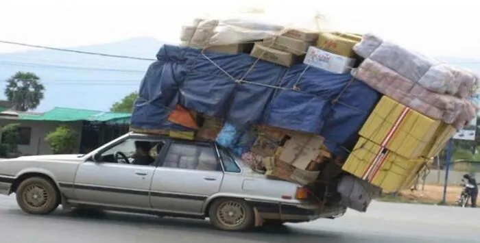 Car overloaded with moving boxes and furniture tipping backward on street