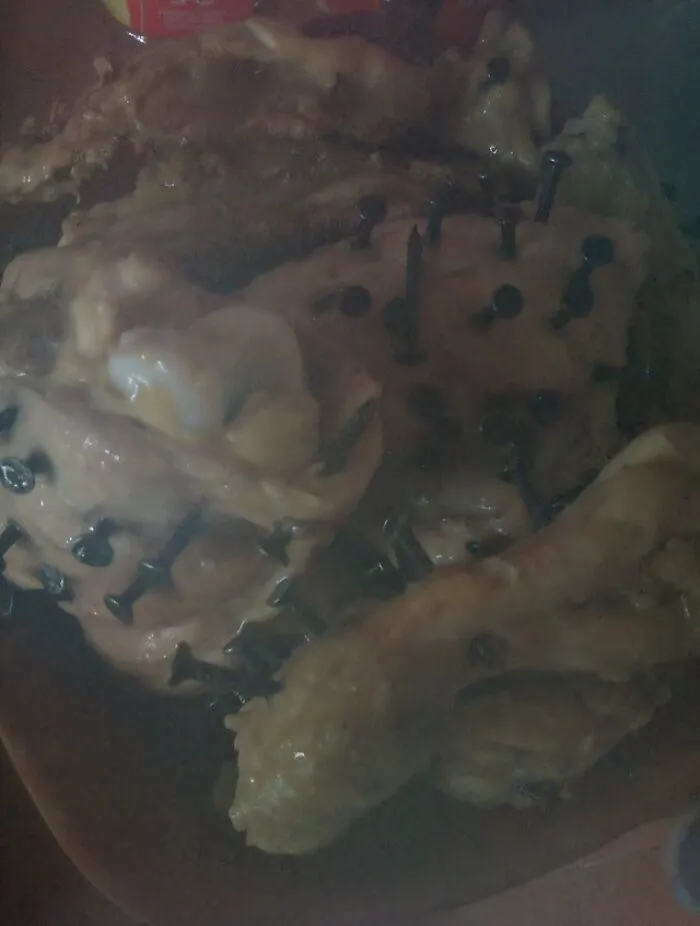 Raw chicken pieces pierced with metallic nails, showcasing extreme and unsafe food combinations.