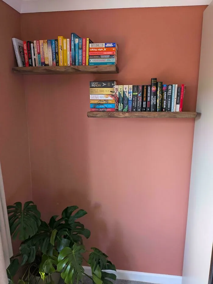 Floating wooden bookshelves installed as smart DIY home upgrades on a terracotta wall.