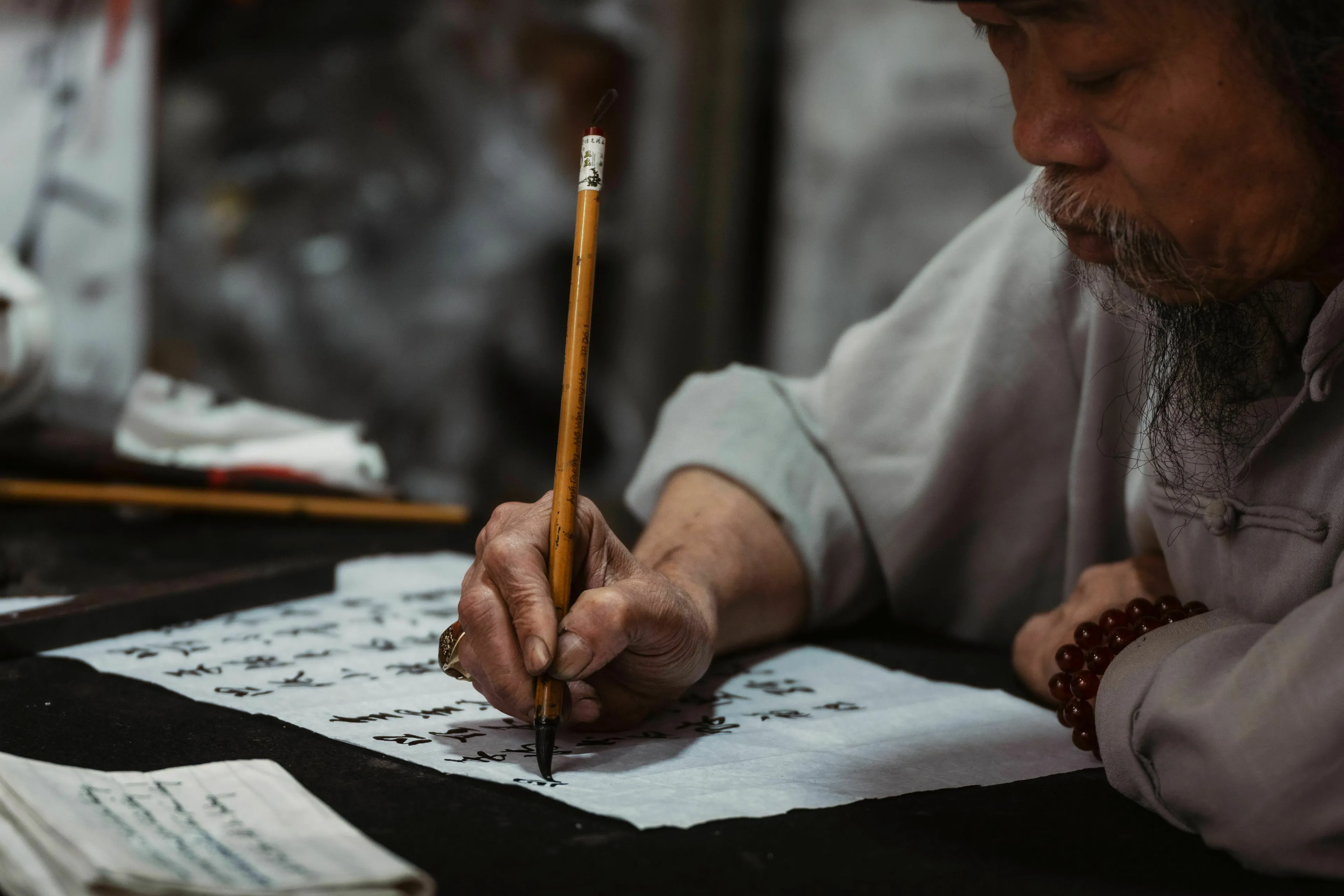 An artist carefully writing characters on paper using a traditional ink brush.