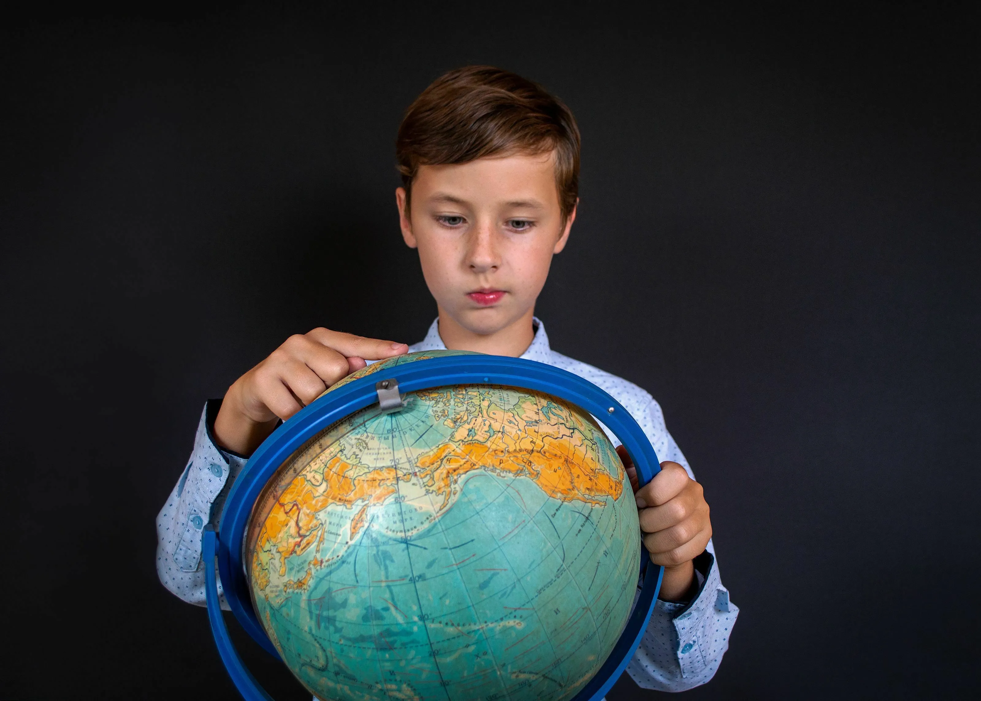 A young boy looking closely at a desk globe, finding a city located on two different continents.
