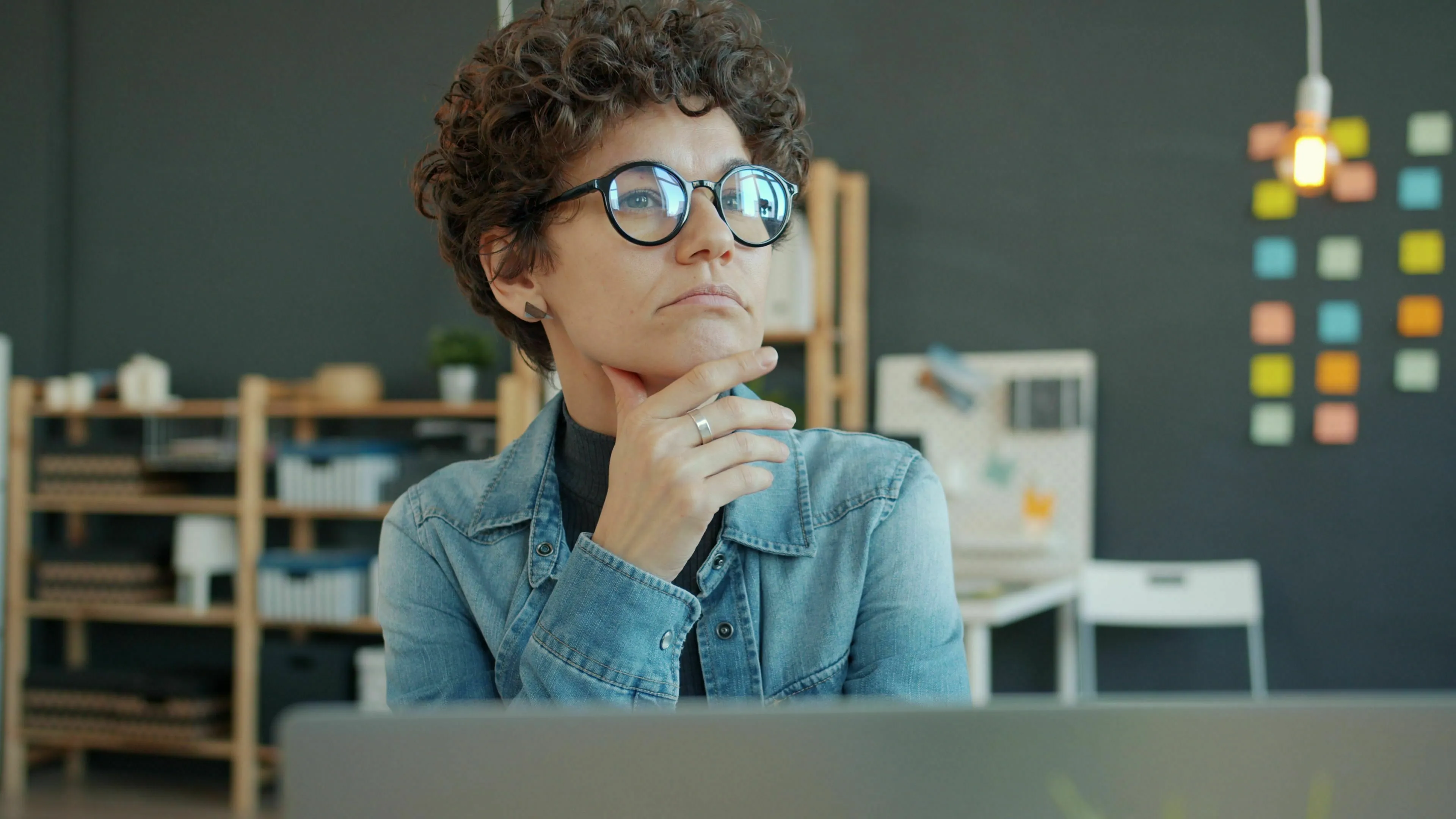 A thoughtful woman wearing glasses looking sideways while pondering a general knowledge question