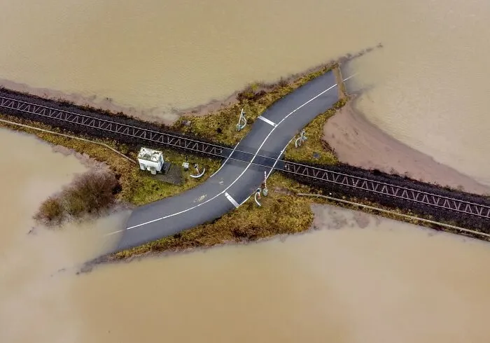 An aerial view of a raised railway and road crossing surrounded by floodwaters, illustrating best infrastructure