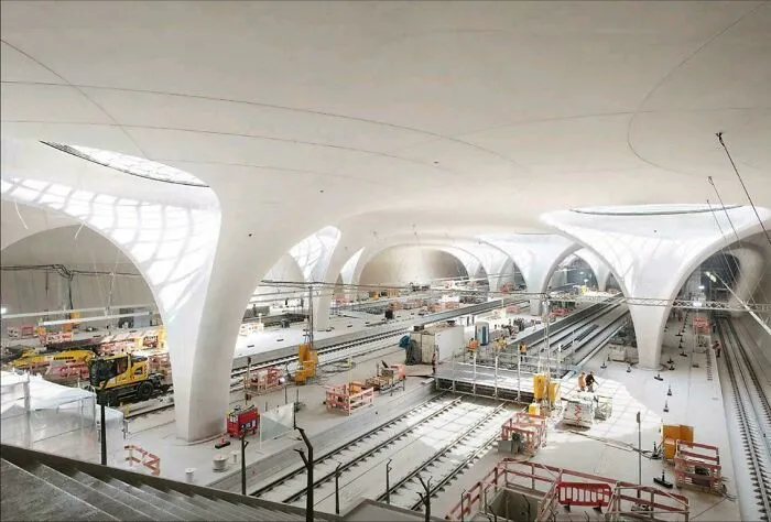 A modern underground train station under construction with large white organic pillars, showing world infrastructure