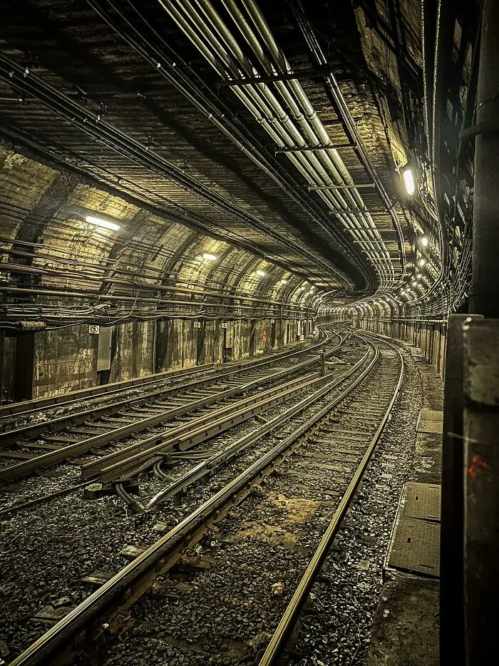 Subway track infrastructure inside a curved underground railway tunnel with overhead pipes