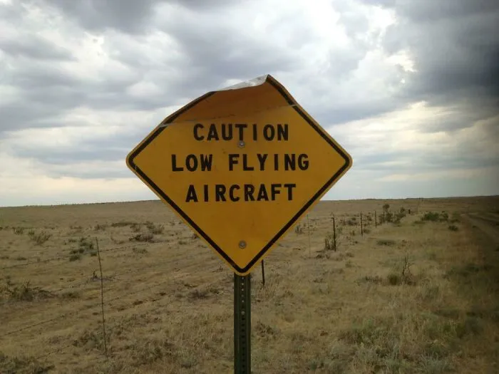 Worn caution sign warning of low flying aircraft in an open field
