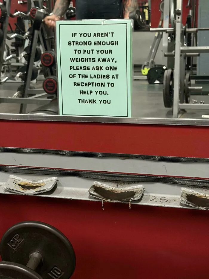 Funny gym sign telling weak people to ask ladies at reception for help putting weights away