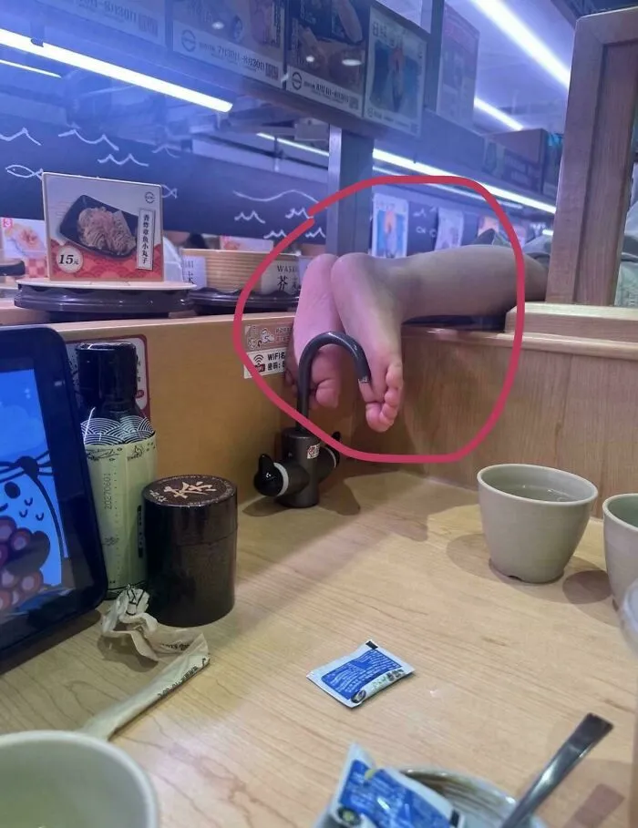 A person with their bare feet resting near a water faucet in a restaurant, showing main character behavior