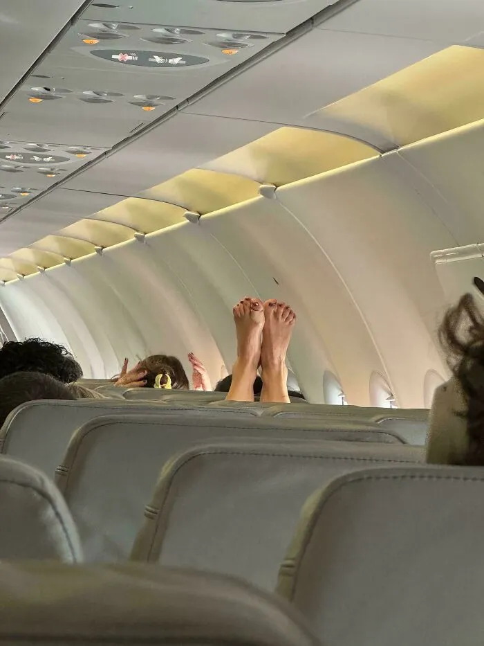 A person resting their bare feet on top of the airplane seat in front of them.
