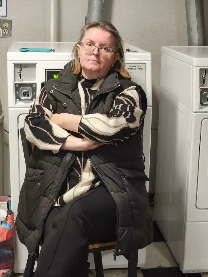 A main character sitting with crossed arms blocking a dryer in a laundry room.