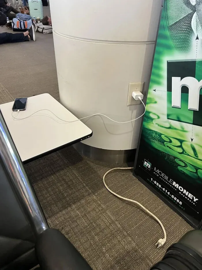 An airport outlet used to charge a phone instead of a nearby advertisement display.