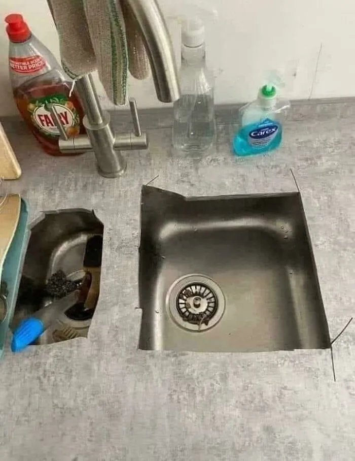 A kitchen countertop with rough, uneven cutouts around the stainless steel sinks.