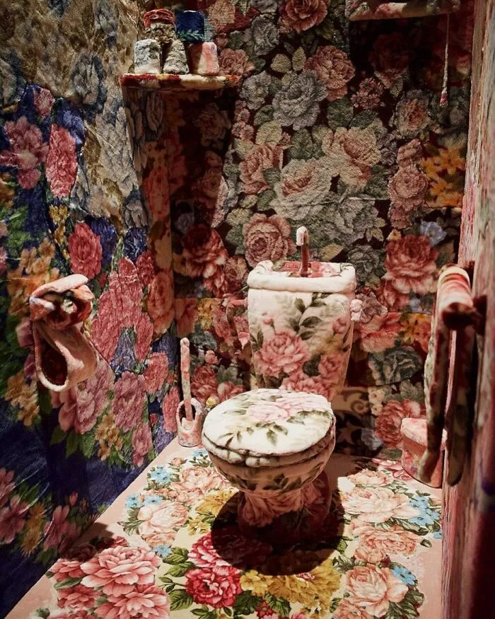 A bathroom completely covered in matching floral carpet, including the toilet, floor, and walls.