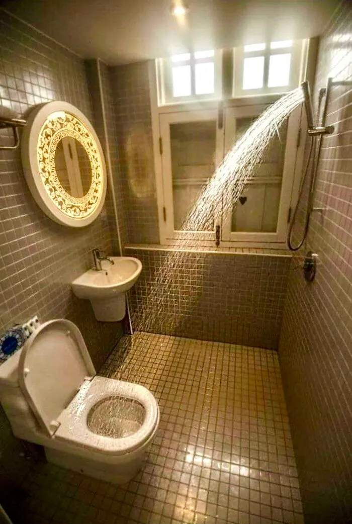 A small bathroom design fail where the shower head sprays water directly onto the open toilet.