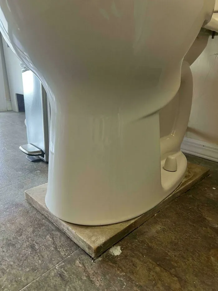 A white toilet propped up on a wooden board as a questionable fix in one of these poorly designed houses.
