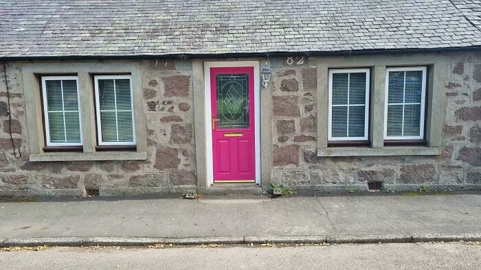 An old stone cottage with an off-center pink front door in houses