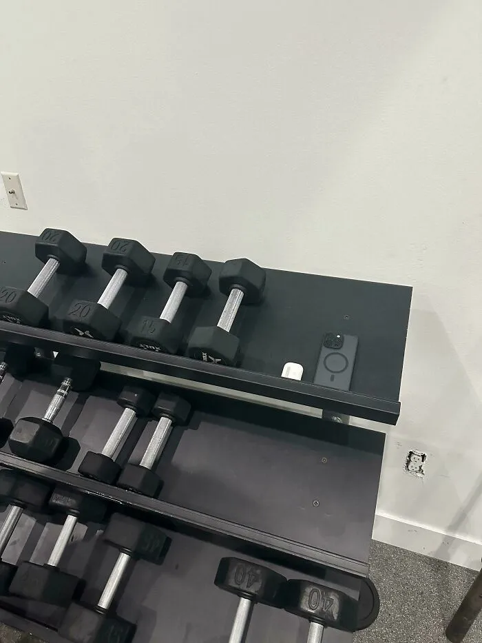 A smartphone and earbuds left on a gym dumbbell rack, illustrating main character behavior