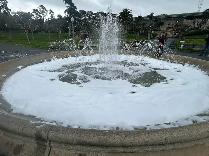 Public fountain filled with thick white soap suds, showing a main character lives prank.