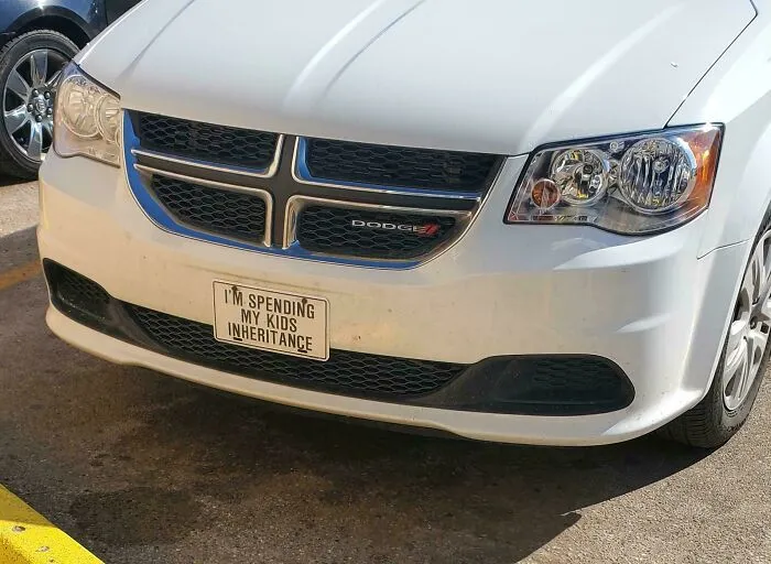 White Dodge vehicle with a license plate reading I am spending my kids inheritance, illustrating main character lives.