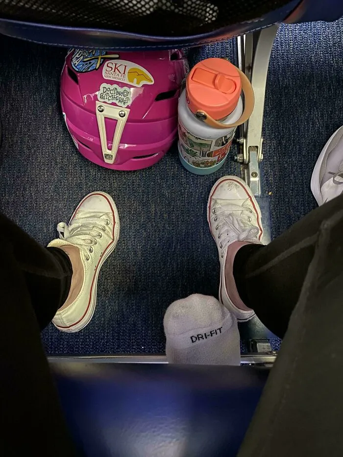 Person displaying main character syndrome by putting bare feet on the headrest in front on an airplane.