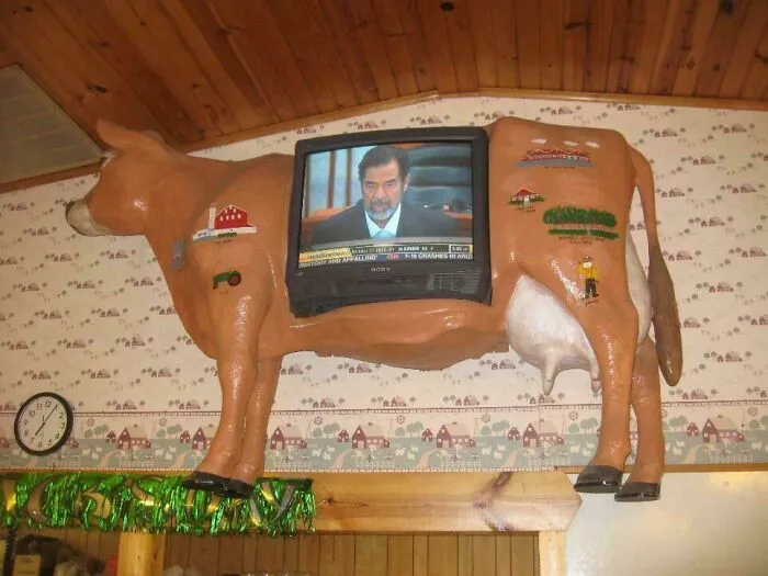 An old television set built into the side of a plastic cow, showcasing bizarre houses decor.