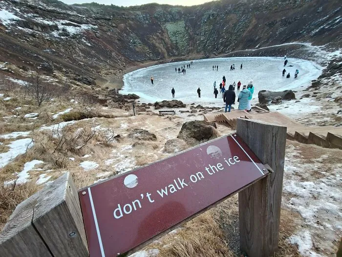 A crowd acting like main characters by ignoring the warning sign and walking onto dangerous thin ice.