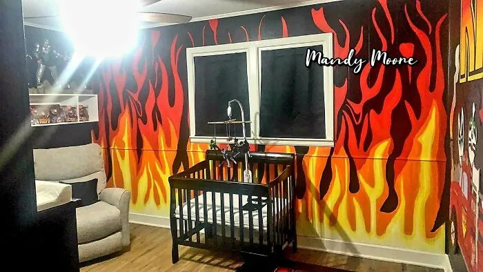 A baby nursery room featuring dark walls painted with large bright flames, demonstrating questionable design choices.