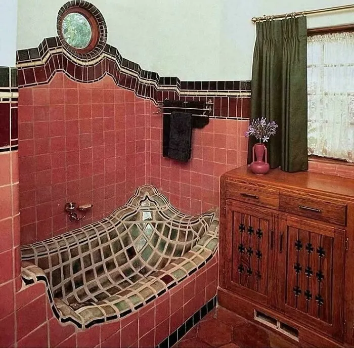 An oddly tiled bathtub design featuring uneven curves and red walls, showcasing questionable house style.