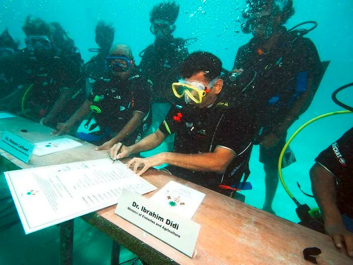 Maldivian cabinet ministers wearing scuba gear and signing documents at an underwater meeting.