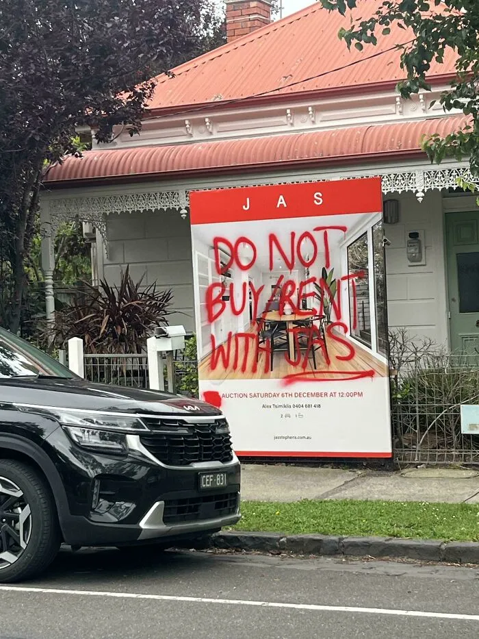 A real estate sign spray-painted with warning graffiti warning against renting and booking with JAS