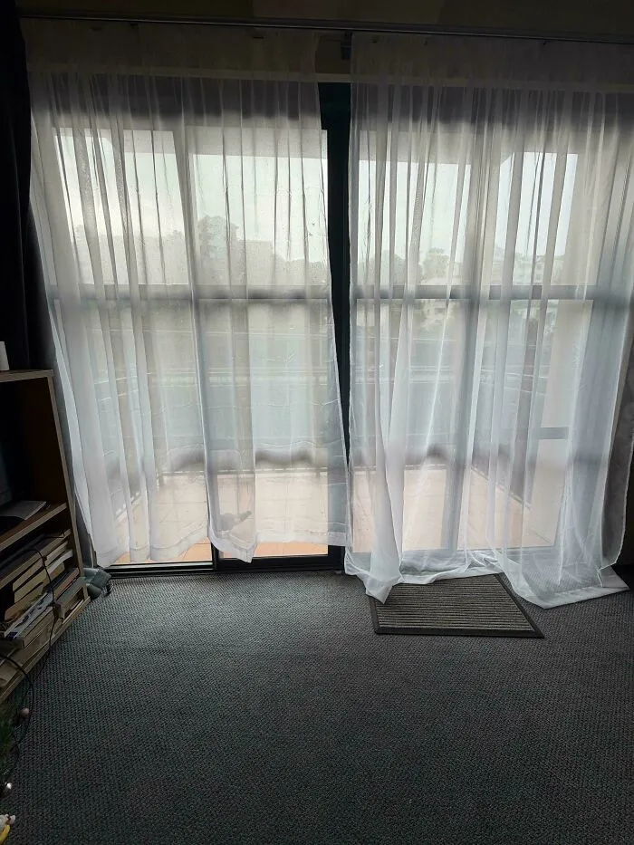 Sheer curtains hanging unevenly on a sliding door in a renting and booking apartment