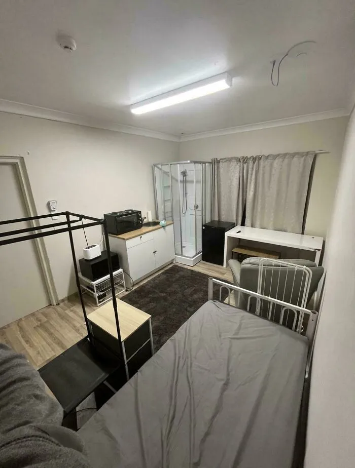 A poorly laid out studio apartment with a bed next to a kitchen and shower, showing a bad renting experience.